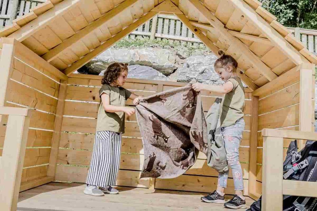 Waldgeburtstag: Zwei Mädchen machen es sich mit einer Decke in der Picknickhütte gemütlich