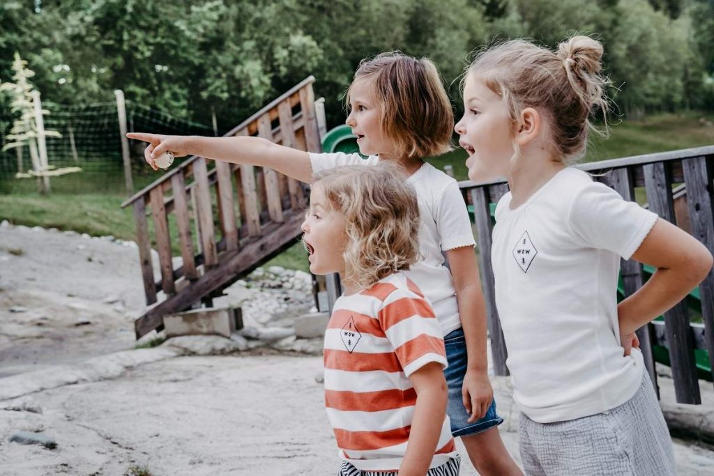 Drei Kinder nehmen am Waldgeburtstag teil und stehen am Spielplatz des Waldparks. Sie zeigen voller Begeisterung in die Ferne.