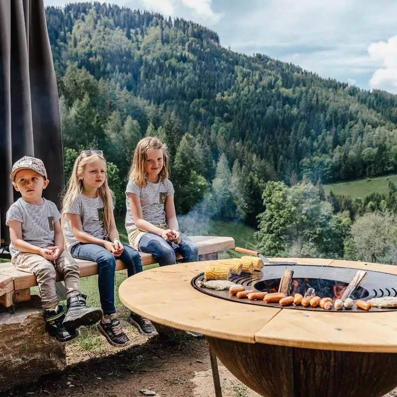 Grillen mit Aussicht für Kindergeburtstag mit 3 Kindern, die gespannt auf ihre Würstchen und Maiskolben warten